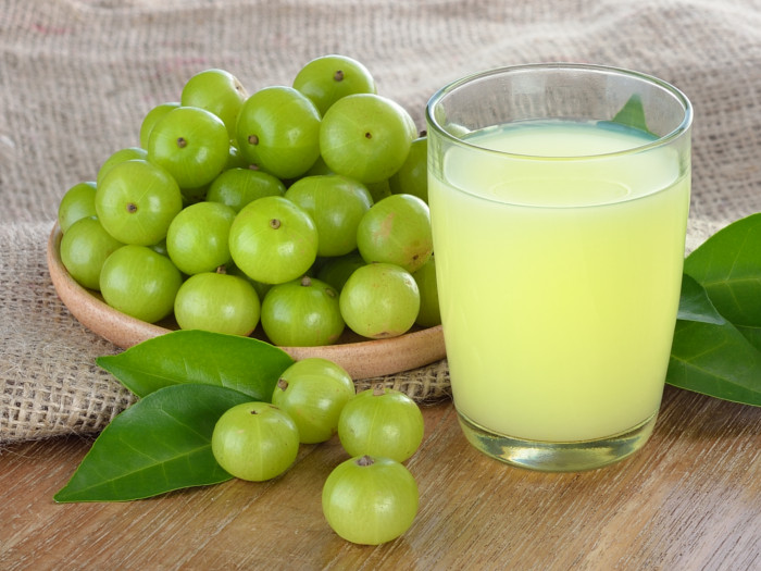 A glass of fresh amla juice kept next to a bowl of amlas