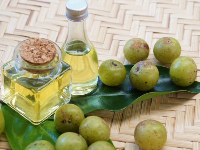 2 bottles of amla oil with fresh amla and leaves on a mat