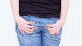 A young woman in tshirt and jeans suffering from symptoms of anal itching