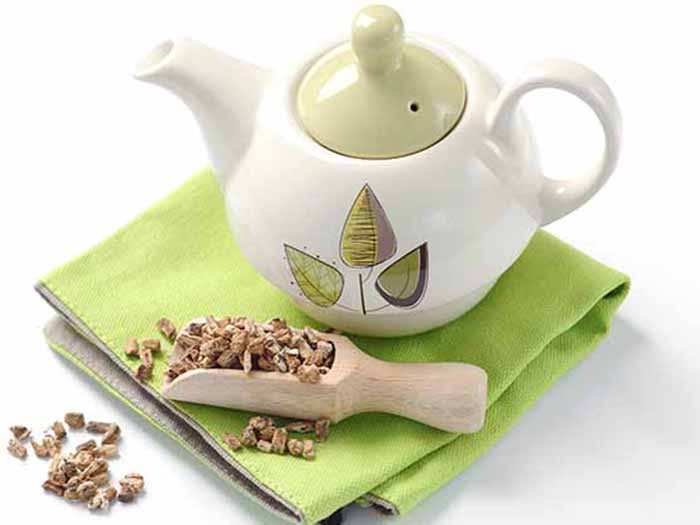 Pot of tea with a scoop of dried roots on a green napkin.