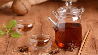 Glass kettle and two cups filled with anise tea, anise leaves, and anise seeds on a wooden table