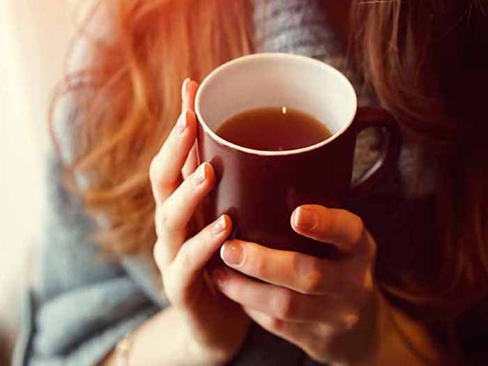 A girl wearing woolen holding a cup of tea in her hands