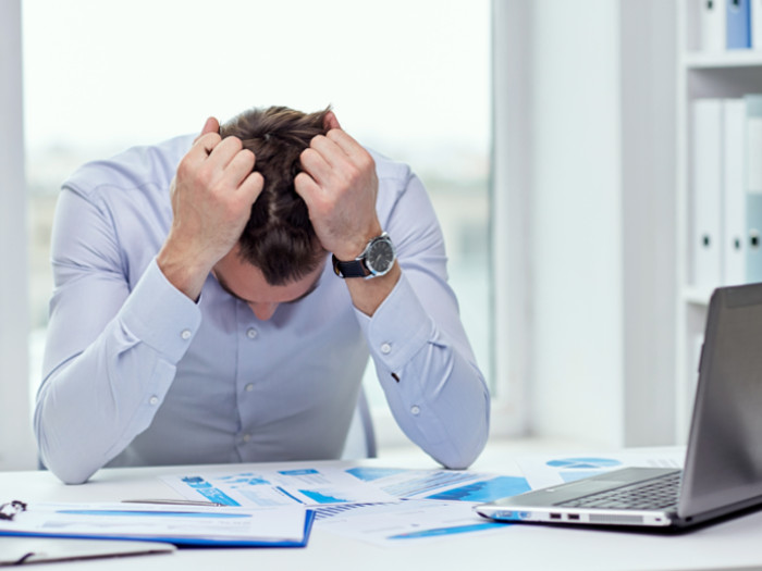 A man sitting at his work desk, looking down, with his hands pulling his hair