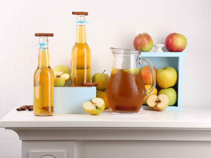 Bottles of apple cider vinegar placed amidst apples against a white background