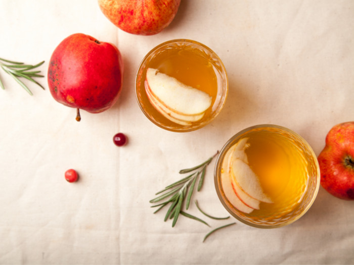 Apple cide vinegar in two glasses next to apples on a white counter-top