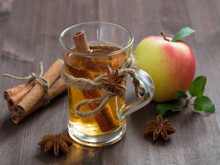 A glass of apple cider vinegar tea with cinnamon, star anise, and apples in the background