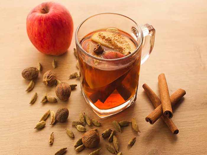 A glass of apple cinnamon tea, kept next to an apple and cinnamon sticks