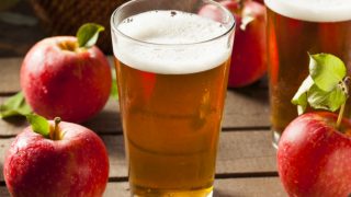 A glass of apple juice with apples next to it