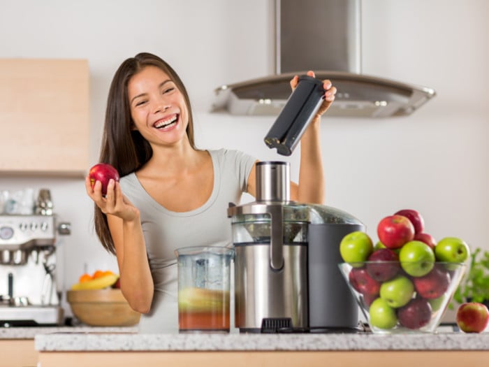 A woman in a modern kitchen making fresh apple juice with a juicer, and green and red apples