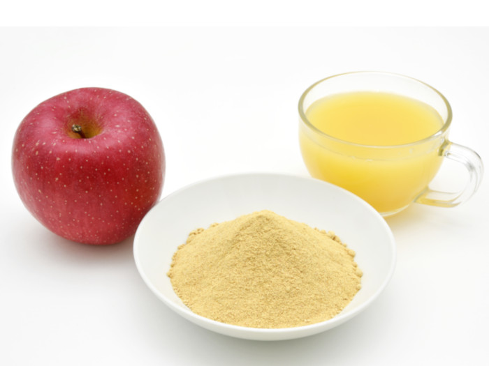 A plate of powder, apple and a cup of yellow-colored liquid placed on a white surface