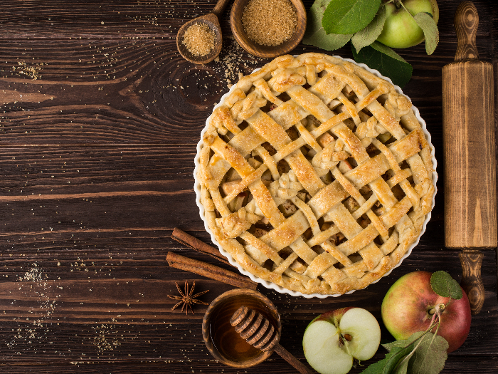 A flat lay picture of an apple pie and ingredients on a wooden background