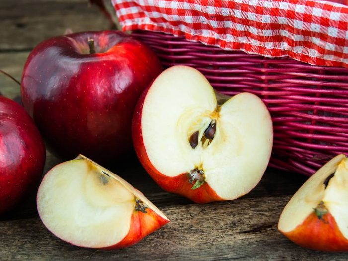 Cut apples kept next to a basket and whole apples atop a wooden platform