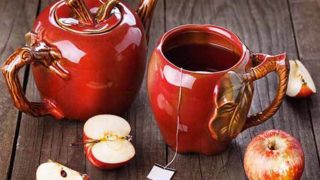 Apple tea in apple-shaped teapot set, with fresh apples on a wooden counter