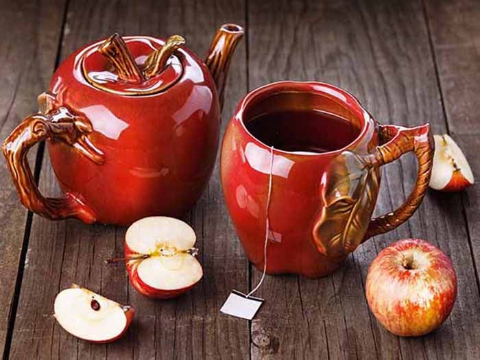 Apple tea in apple-shaped teapot set, with fresh apples on a wooden counter