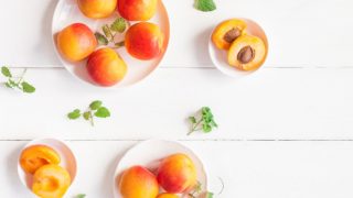 2 big bowls of whole apricots (ripe) and 2 small bowls of half apricots (ripe) with and without seeds on a white table