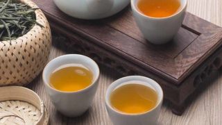 Chinese set of teapot and teacups with green tea and green tea leaves in a basket