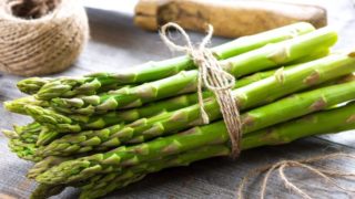 A bunch of fresh green asparagus, rope, and knife on a wooden table