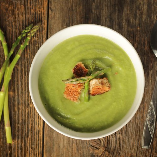 Top view of a asparagus soup in a white bowl on a rustic background