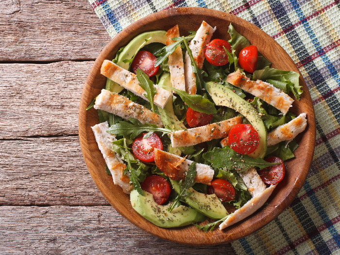 Chicken salad with avocado, arugula and cherry tomatoes in a wooden plate.