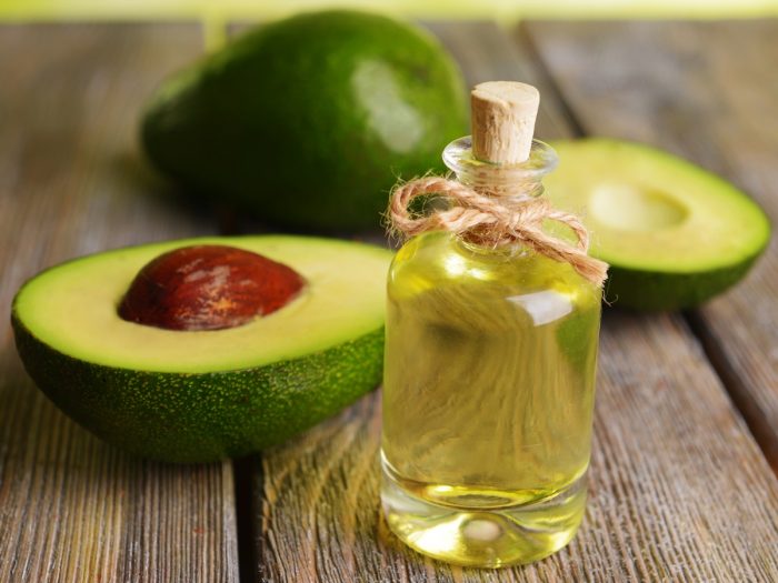 A close-up shot of avocado oil placed in front of sliced avocados