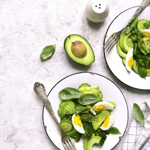 A flat lay picture of two portions of green detox salad with avocado,broccoli,cucumber and eggs on a light slate,stone or concrete background