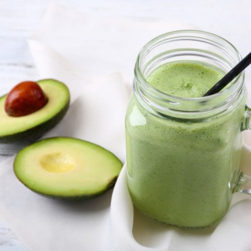 Avocado smoothie in a mason jar with a cut avocado in the background