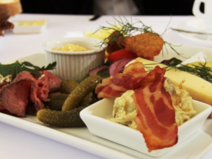 Delicious bacon placed alongside pickle and cheese, atop a bowl of mashed potatoes