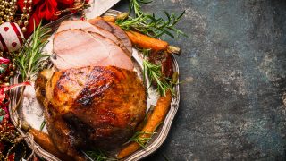 Roasted sliced Christmas ham on plate with fork, knife and festive decoration against a dark rustic background