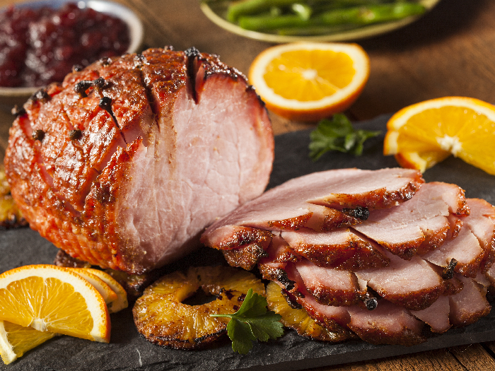 Roasted sliced Christmas ham on plate with fork, knife and festive decoration against a dark rustic background