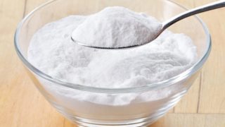 Close up of a glass bowl and spoon filled with baking soda on a wooden table