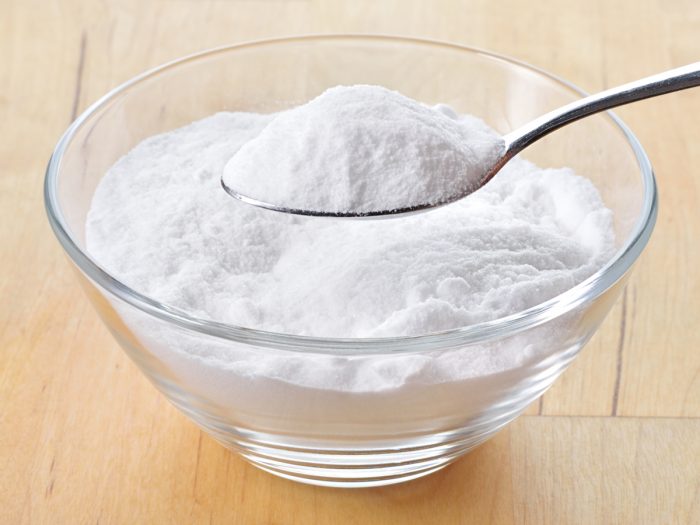 Close up of a glass bowl and spoon filled with baking soda on a wooden table