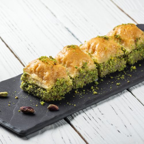 Turkish baklava turkish delight, oriental sweets on a black dish for serving on a wooden white table.