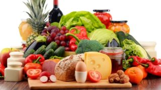 A picture representing a balanced diet with fruits, vegetables, oil, cheese, bread, egg, and nuts.