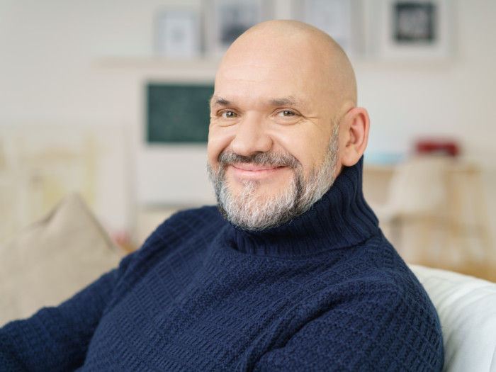 An older bald man sitting and smiling into the camera