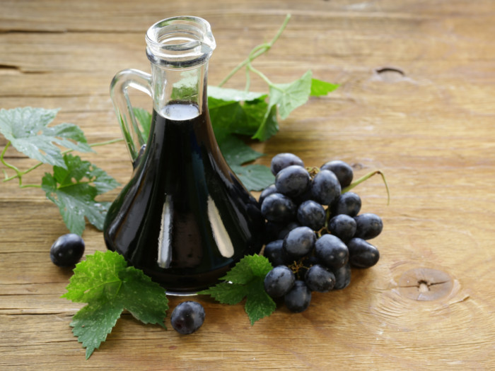 Balsamic vinegar in a bottle with grapes and grape leaves on a wooden surface