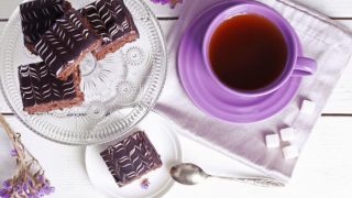 Banaba tea in a purple cup, next to chocolate brownies, banaba flowers, and sugar cubes