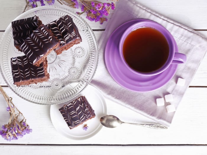 Banaba tea in a purple cup, next to chocolate brownies, banaba flowers, and sugar cubes