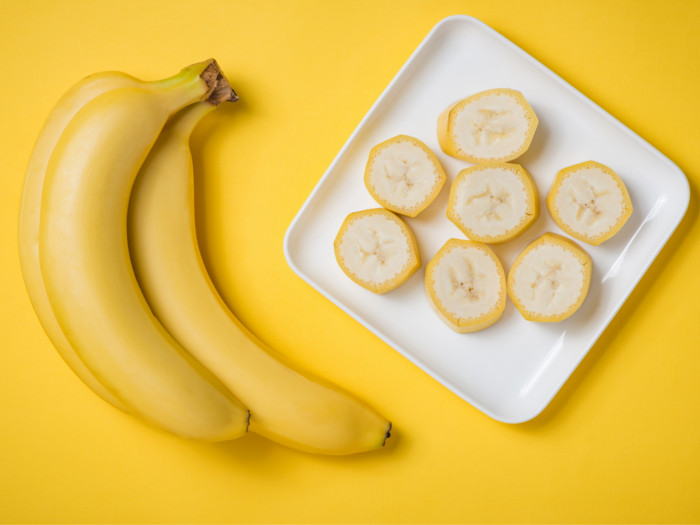 Sliced bananas on a plate with two whole bananas aside