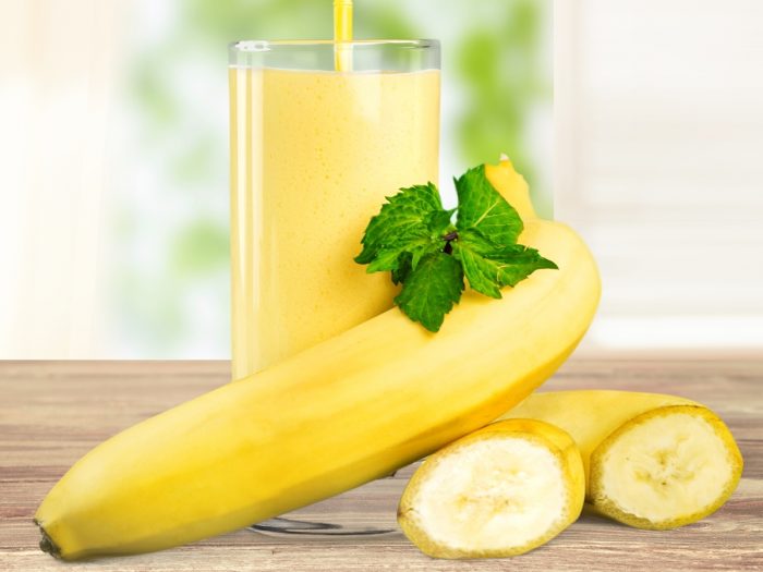 A glass of banana juice, kept next to bananas, atop a wooden table