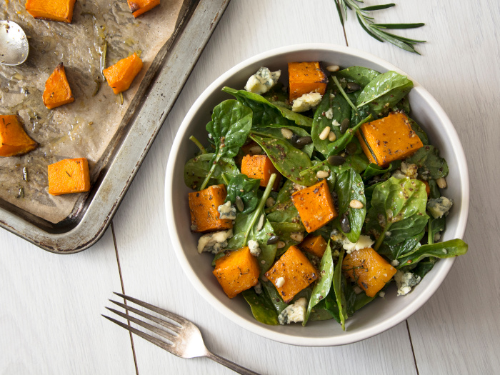 Squash, spinach, and pine nuts salad in a white bowl