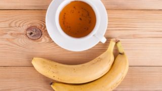A cup of banana tea with fresh ripe bananas on a wooden table