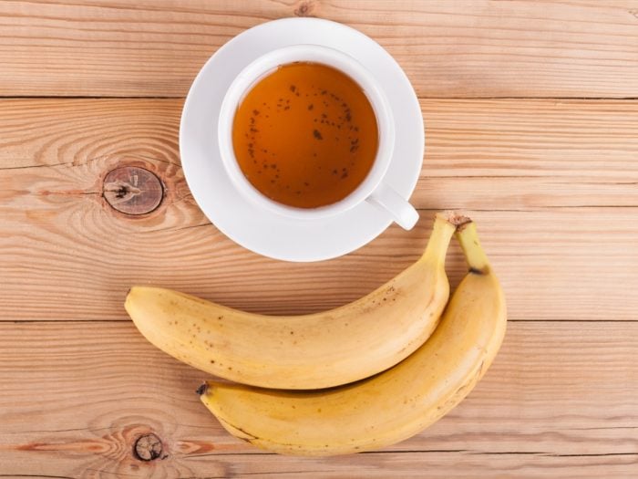 A cup of banana tea with fresh ripe bananas on a wooden table