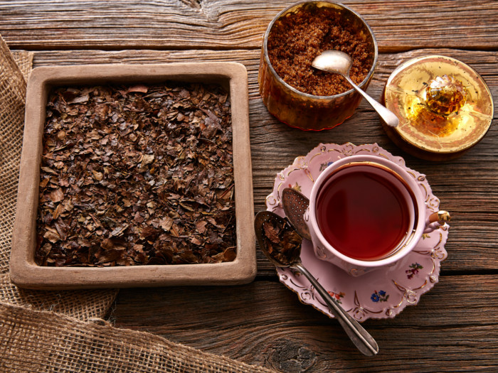 A cup of bancha tea kept next to a tray of dried bancha leaves, atop a wooden table