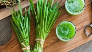 2 fresh bunches of young barley grass with 2 glasses of barley grass juice on a wooden table