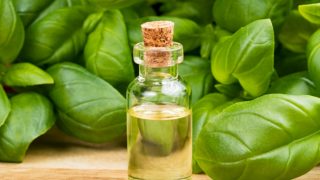 A small bottle of basil oil and fresh basil leaves on a wooden table