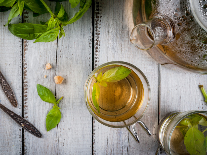 Basil tea in a cup and basil leaves on a wooden counter