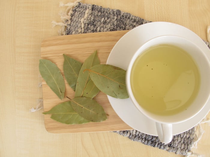 A flat lay pic of bay leaf tea in a white cup places on a wooden platform, right next to a bunch of bay leaves