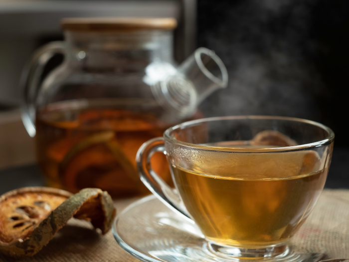 A cup of bael tea, teapot, and slices of dried bael fruit