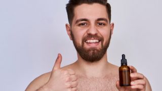 A young smiling man holding a bottle of essential oil