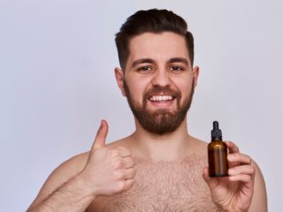 beardoil A young smiling man holding a bottle of essential oil